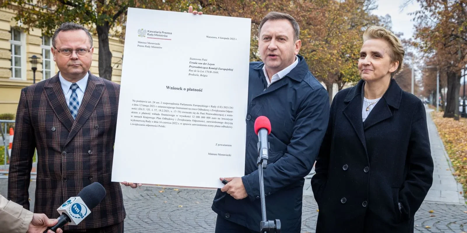 Na zdjęciu trzej urzędnicy, w tym jeden trzymający dokument, prezentują wniosek o płatność związany z funduszami europejskimi.