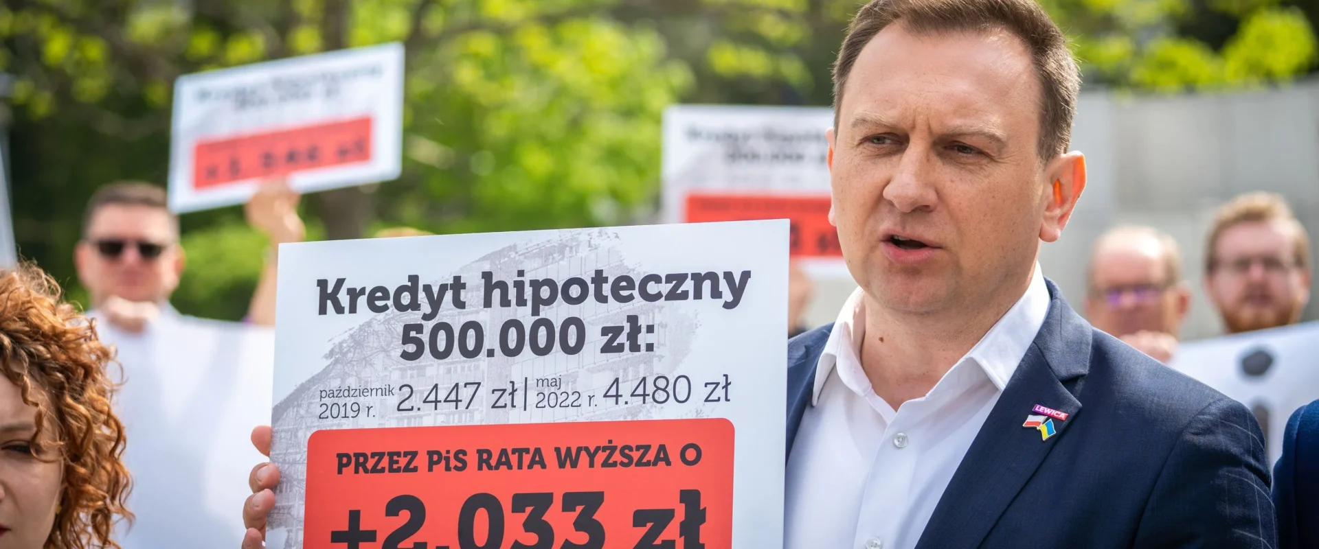 Osoba trzymająca plakat informujący o wzroście raty kredytu hipotecznego w Polsce, podczas wydarzenia politycznego.