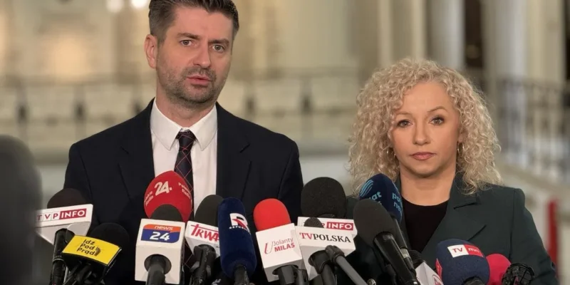 Dwóch przedstawicieli przemawia na konferencji prasowej, stojąc za licznymi mikrofonami, w związku z ochroną polskich rodzin przed przemocą.