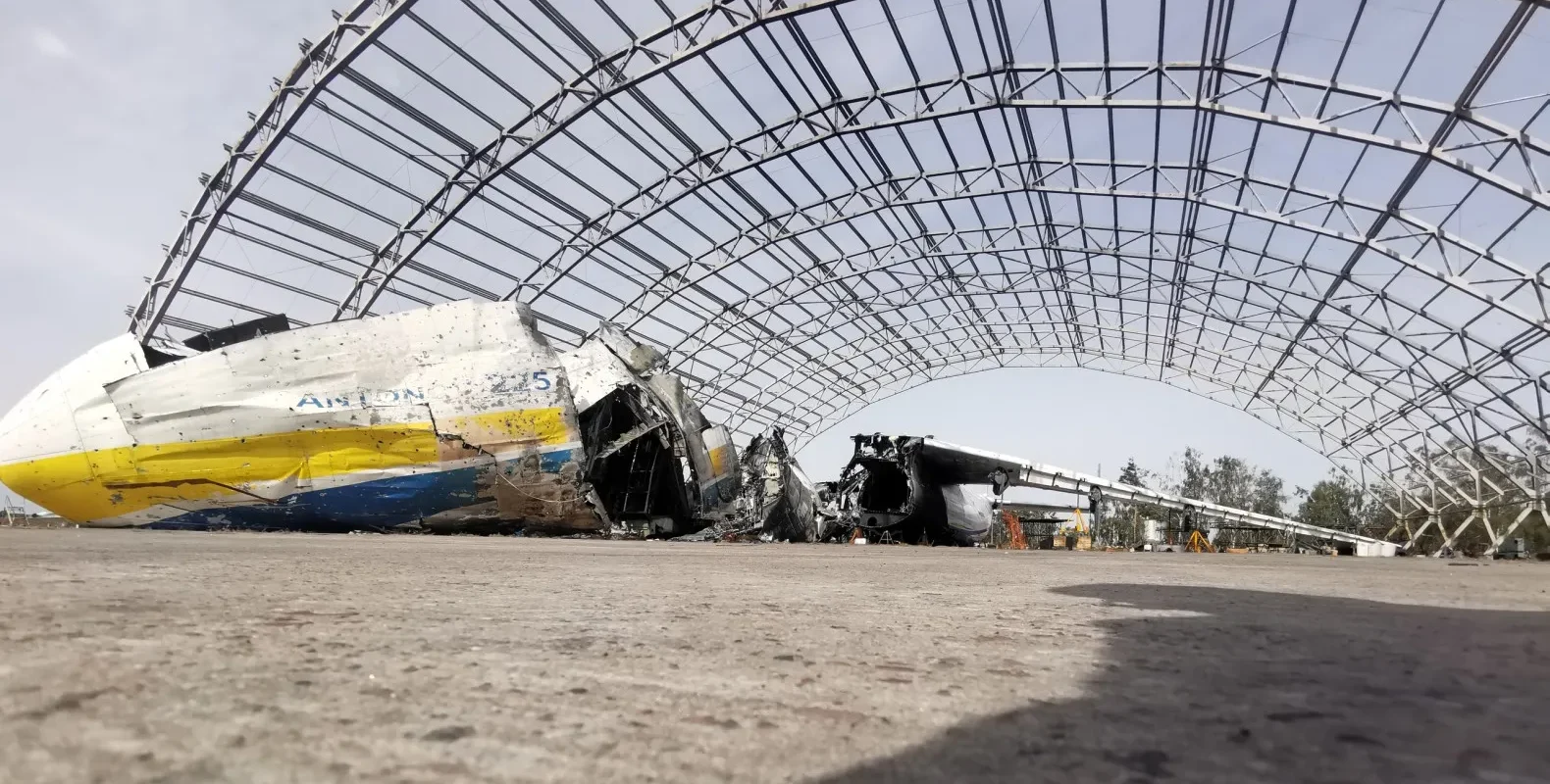 Zniszczony samolot pod ogromną metalową konstrukcją, otoczony przez resztki innego sprzętu lotniczego.