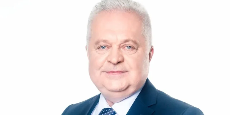 Portret mężczyzny w granatowym garniturze, jasnoniebieskiej koszuli i wzorzystym krawacie na białym tle.