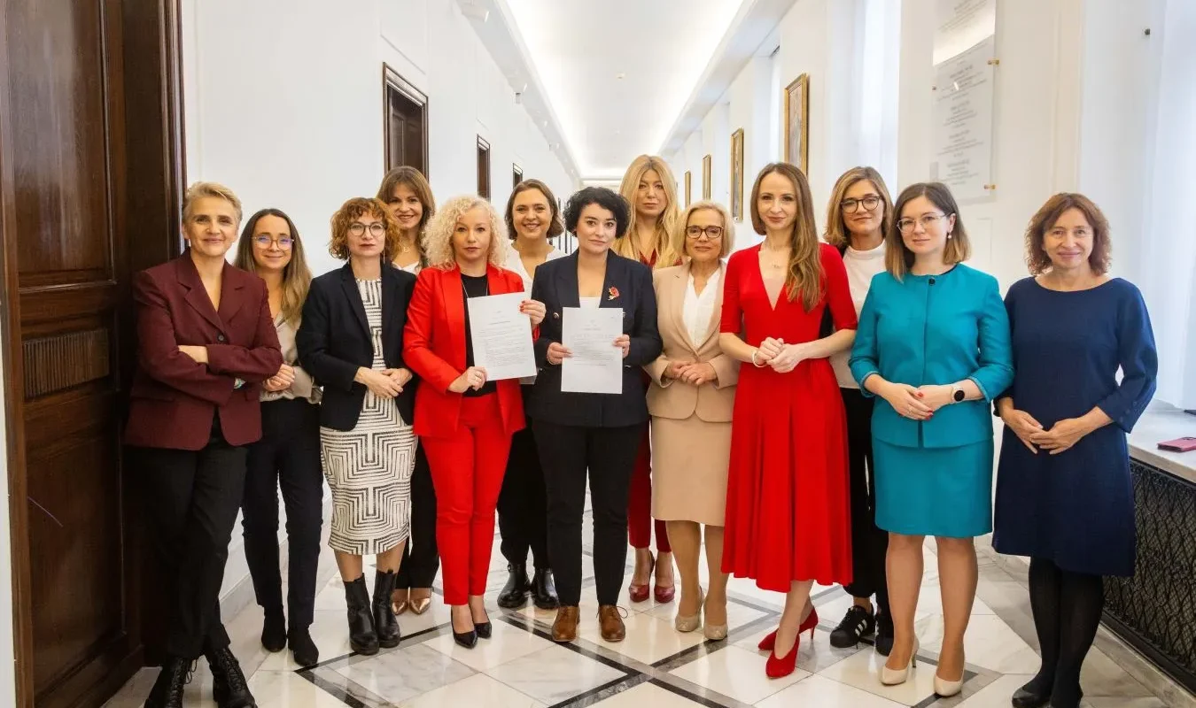 Grupa kobiet w eleganckich strojach stoi w korytarzu i trzyma podpisane dokumenty, prezentując projekty ustaw Lewicy dotyczące liberalizacji prawa aborcyjnego i depenalizacji aborcji.