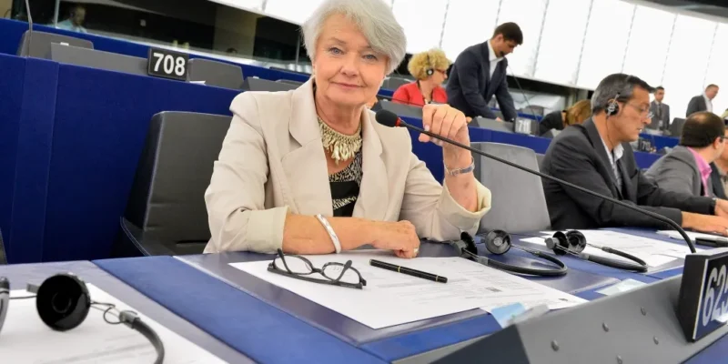 Kobieta w jasnej marynarce siedzi przy stanowisku w sali plenarnej Parlamentu Europejskiego, trzymając mikrofon i patrząc w stronę kamery.