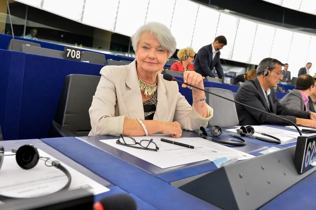 Kobieta w jasnej marynarce siedzi przy stanowisku w sali plenarnej Parlamentu Europejskiego, trzymając mikrofon i patrząc w stronę kamery.