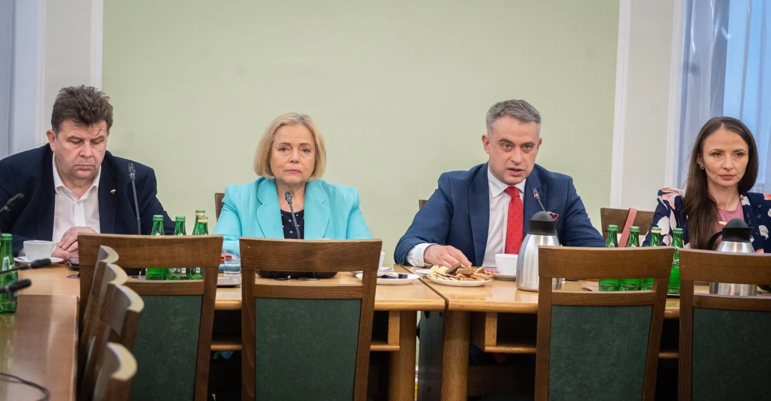 Cztery osoby w formalnych ubraniach siedzą przy stole konferencyjnym podczas spotkania dotyczącego strategii na srebrną rewolucję, z zielonymi butelkami wody i przekąskami na stole.