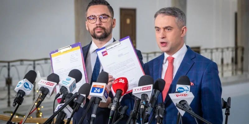 Dwóch mężczyzn stoi przed mikrofonami i przedstawia dokumenty w trakcie konferencji prasowej.