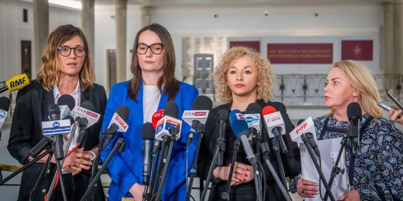 Cztery kobiety w formalnych ubraniach stoją przed zestawem mikrofonów z logotypami polskich mediów podczas konferencji prasowej.