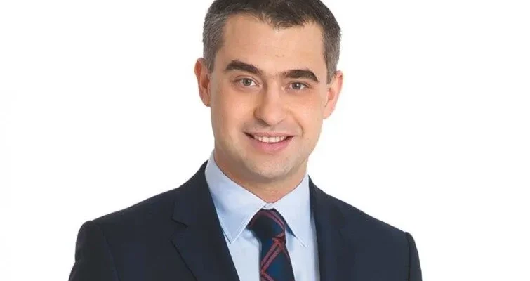 Portret uśmiechniętego mężczyzny w granatowym garniturze i krawacie na białym tle.