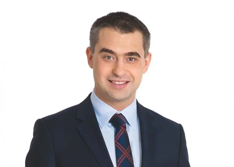 Portret uśmiechniętego mężczyzny w granatowym garniturze i krawacie na białym tle.