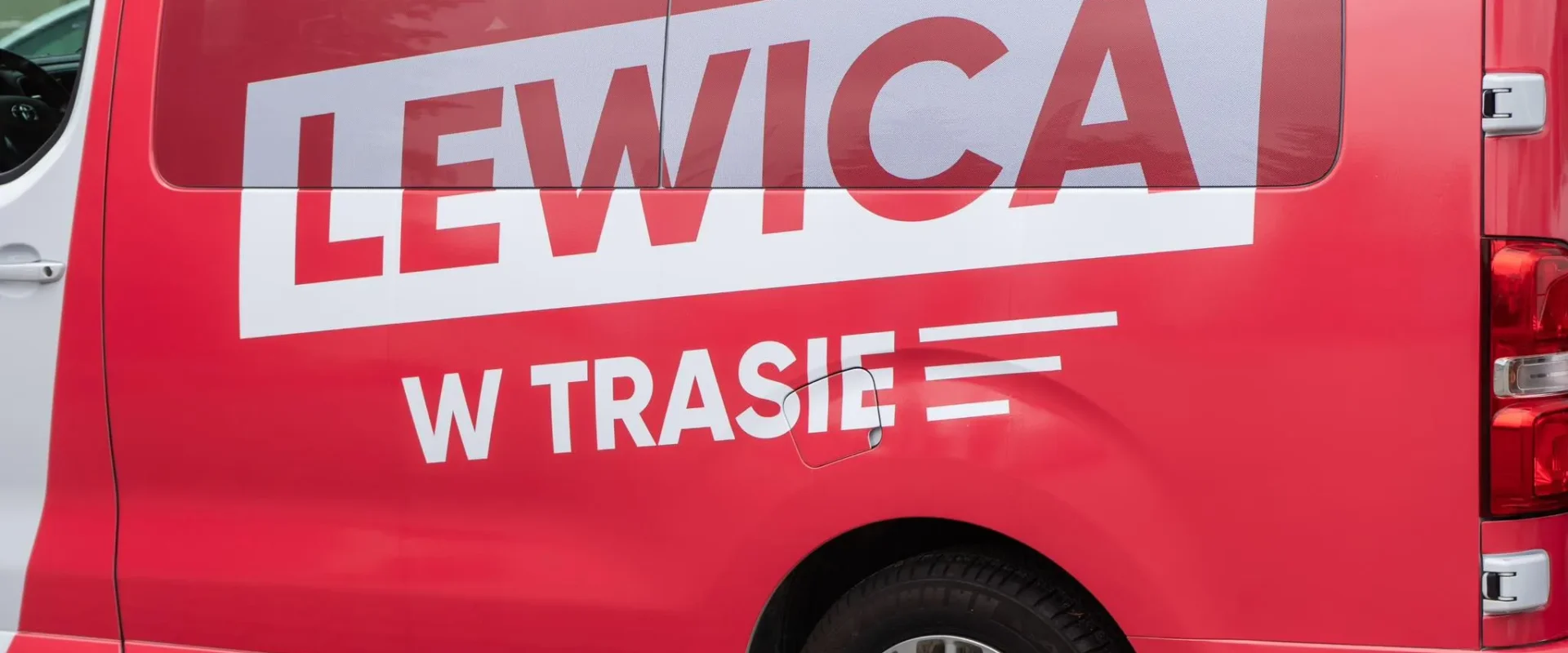 Czerwona furgonetka z dużym białym napisem LEWICA na bocznej ścianie i dodatkowym napisem W TRASIE.