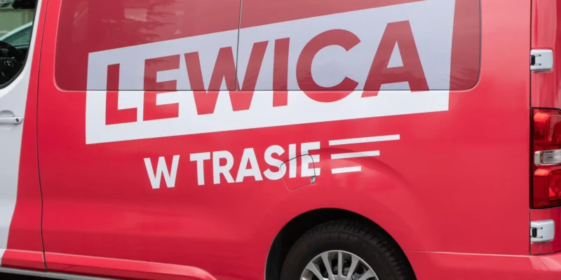 Czerwona furgonetka z dużym białym napisem LEWICA na bocznej ścianie i dodatkowym napisem W TRASIE.