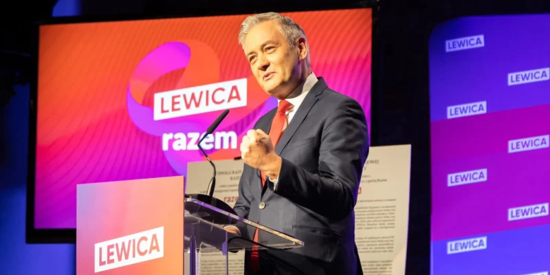 Na zdjęciu widać polityka przemawiającego z mównicy podczas wydarzenia związanego z partią Lewica, z logo „razem” w tle.