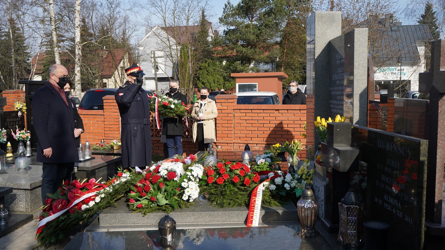 Grupa osób w maseczkach składa wieńce i zapala znicze przy grobie, upamiętniając 11. rocznicę tragedii smoleńskiej.
