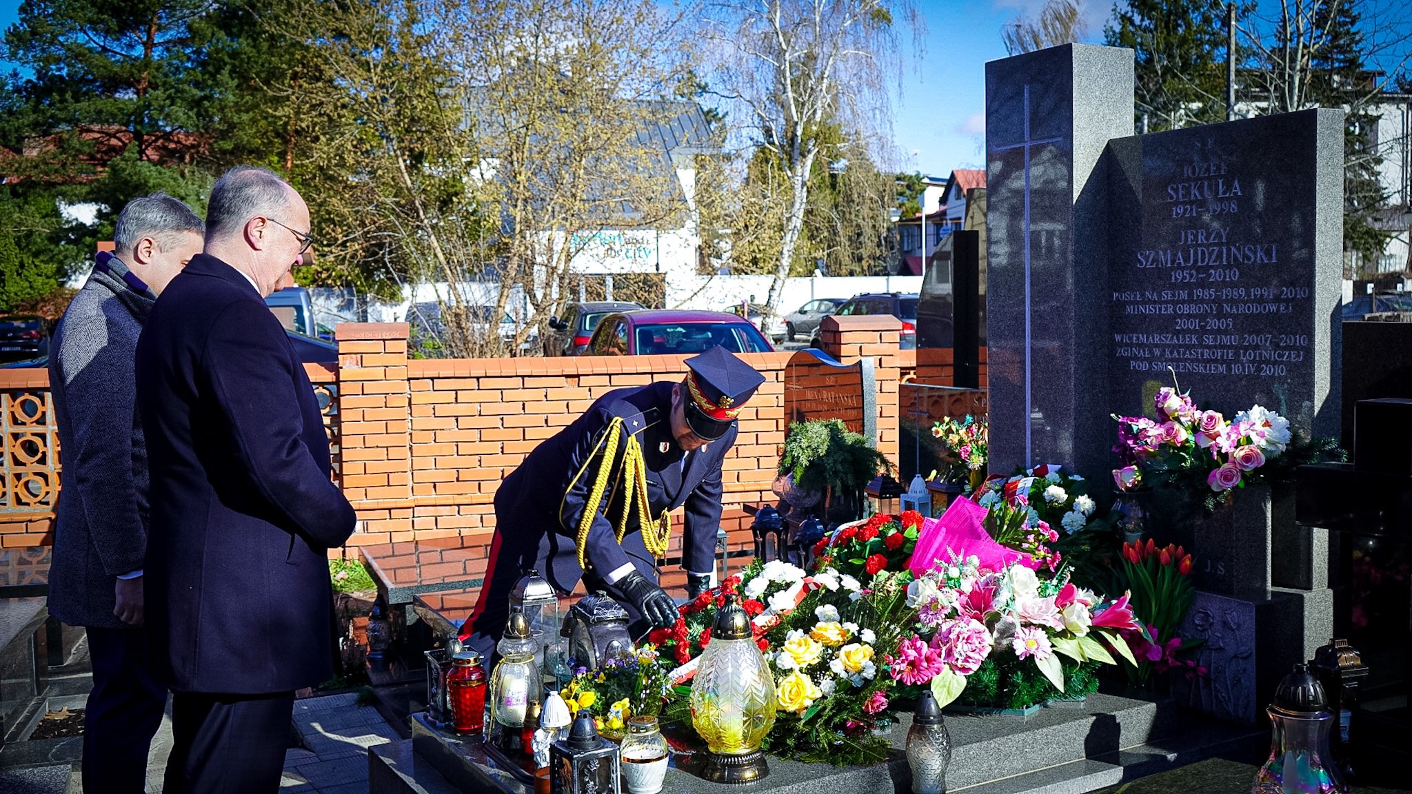 Grupa mężczyzn składa kwiaty i zapala znicze przed granitowym pomnikiem upamiętniającym tragedię smoleńską, w 12. rocznicę tego wydarzenia.