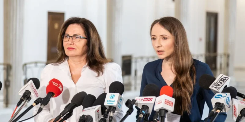 Na zdjęciu widoczne są dwie kobiety stojące przed mikrofonami podczas konferencji prasowej.
