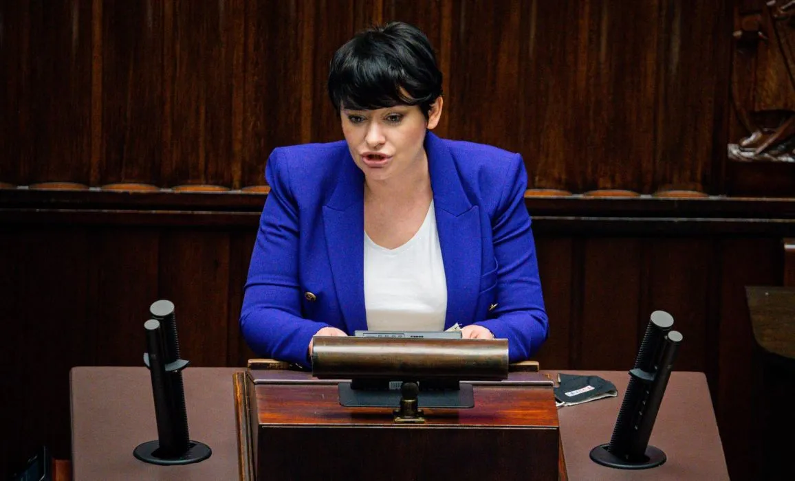 Kobieta w niebieskim żakiecie przemawia z mównicy w sali obrad.