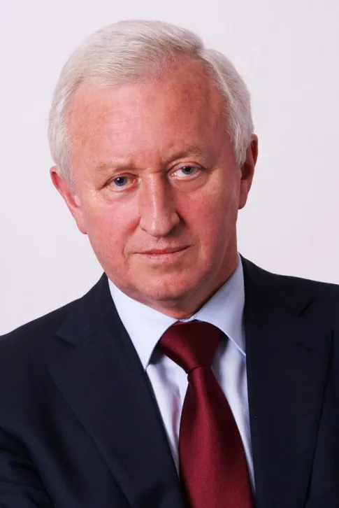 Portret starszego mężczyzny w granatowym garniturze i bordowym krawacie na jasnym tle, ilustrujący artykuł o wpływie Brexitu na budżet UE.