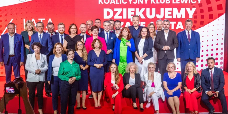 Grupa posłów i posłanek Lewicy stoi na scenie na czerwonym tle z napisem KOALICYJNY KLUB LEWICY, upamiętniając cztery lata działalności Lewicy w Sejmie.