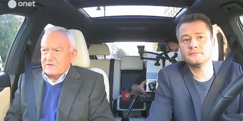 Dwaj mężczyźni siedzą w przednich fotelach samochodu podczas nagrania wywiadu, a za nimi widać kamerzystę z aparatem.