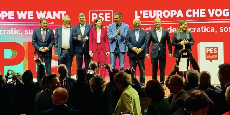 Grupa polityków stoi na scenie podczas wiecu europejskiej socjaldemokracji na czerwonym tle z logiem PSE.