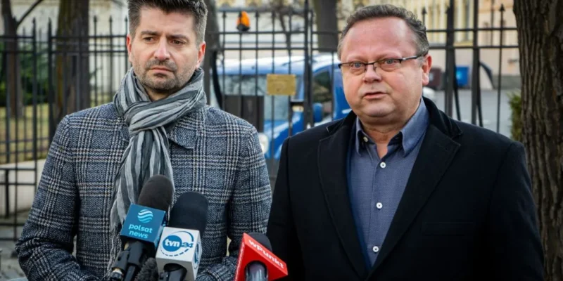 Dwóch mężczyzn stojących przy mikrofonach podczas konferencji prasowej na tle ogrodzenia, omawiających orzeczenie TSUE ws. pieniędzy za praworządność i ochrony funduszy unijnych przed rozkradaniem.