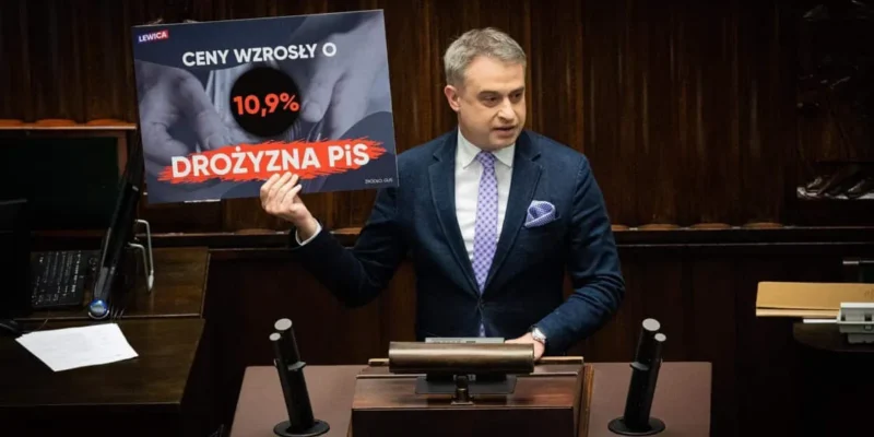 Na zdjęciu przedstawiony jest mężczyzna w garniturze, który trzyma plakat informujący o wzroście cen o 10,9% oraz wskazujący na drożyznę, podczas wystąpienia w sejmie.