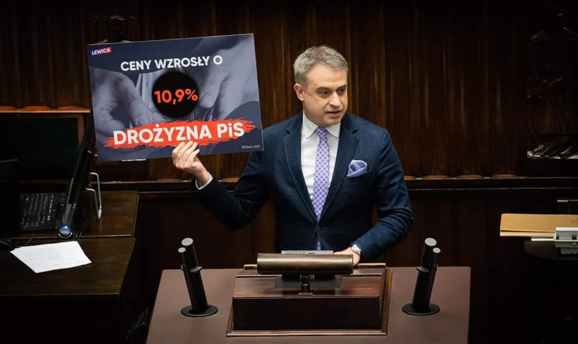 Na zdjęciu przedstawiony jest mężczyzna w garniturze, który trzyma plakat informujący o wzroście cen o 10,9% oraz wskazujący na drożyznę, podczas wystąpienia w sejmie.