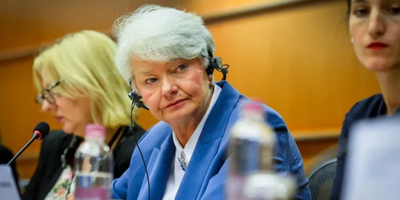 Kobieta w niebieskiej marynarce z zestawem słuchawkowym siedzi przy stole obrad Komisji Kultury i Edukacji, słuchając dyskusji.