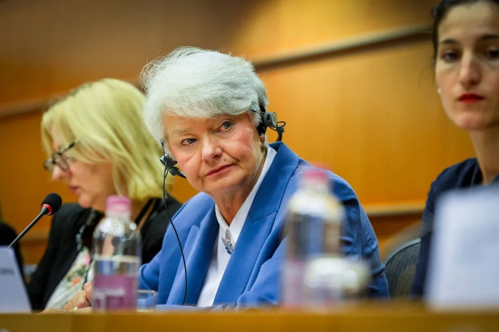 Kobieta w niebieskiej marynarce z zestawem słuchawkowym siedzi przy stole obrad Komisji Kultury i Edukacji, słuchając dyskusji.