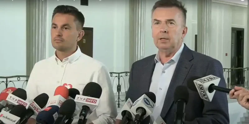 Dwóch mężczyzn, reprezentantów Lewicy i Koalicji Obywatelskiej, udziela konferencji prasowej, stojąc przy szeregu mikrofonów z logotypami stacji telewizyjnych w eleganckim wnętrzu.