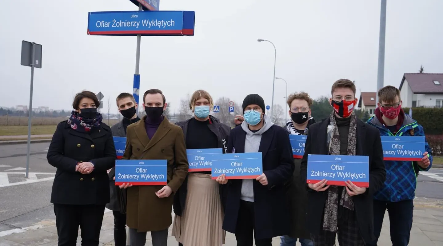 Grupa osób stojących na ulicy trzyma tablice z napisem „Ofiar Żołnierzy Wyklętych”, upamiętniając ofiary i wyrażając sprzeciw wobec równania bohaterów z mordercami.