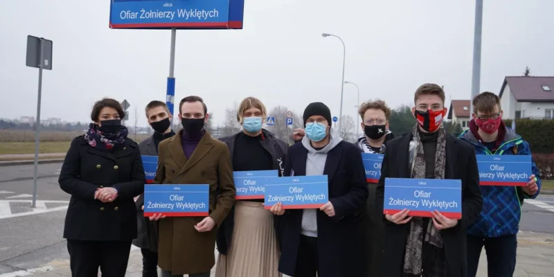 Grupa osób stojących na ulicy trzyma tablice z napisem „Ofiar Żołnierzy Wyklętych”, upamiętniając ofiary i wyrażając sprzeciw wobec równania bohaterów z mordercami.