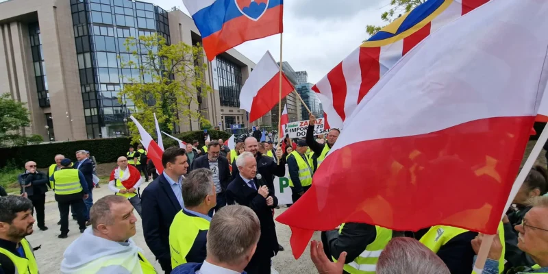 Na zdjęciu widoczna jest demonstracja z udziałem osób w kamizelkach odblaskowych, trzymających flagi Polski i Słowacji, odbywająca się w miejskim otoczeniu.