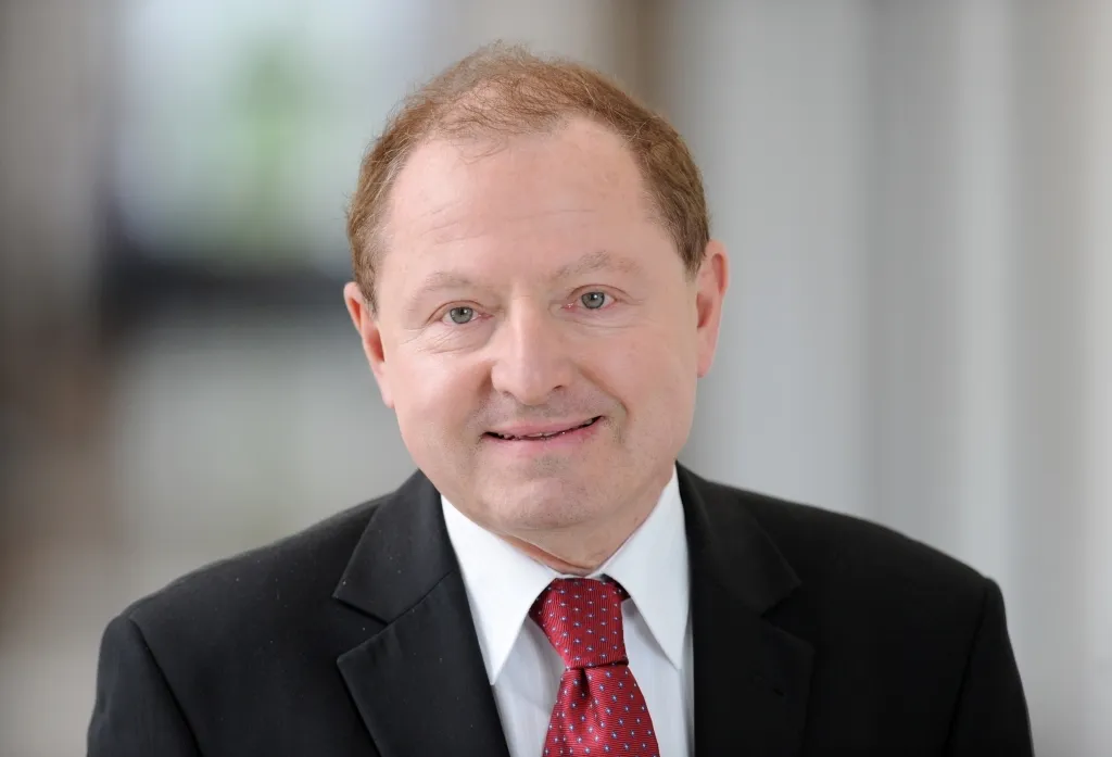 Mężczyzna w garniturze i czerwonym krawacie patrzy prosto w obiektyw i uśmiecha się.