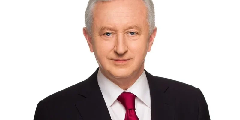 Portret mężczyzny w ciemnym garniturze, białej koszuli i bordowym krawacie na białym tle.