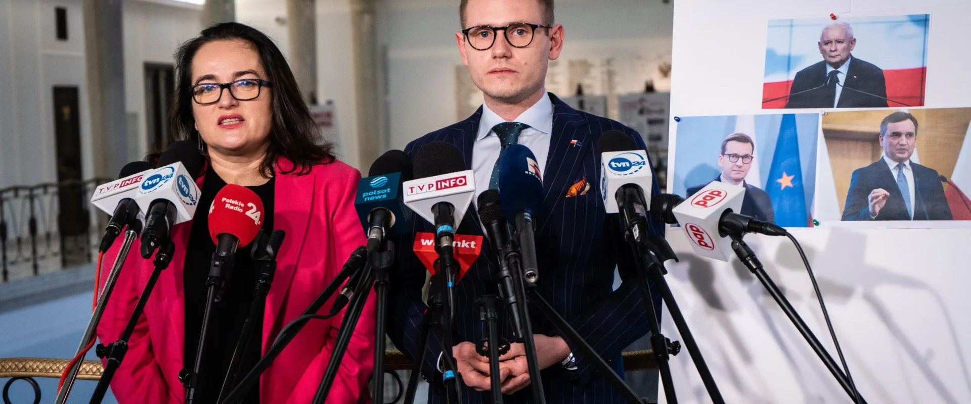 Dwóch polityków stoi przy zestawie mikrofonów podczas konferencji prasowej, obok planszy z fotografiami i napisem „ZAKŁADNICY MEJZY”.