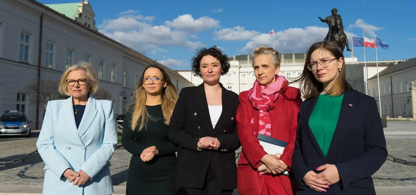 Pięć posłanek Lewicy stoi na placu przed budynkiem z posągiem i flagami, ubranych w eleganckie marynarki, podczas wydarzenia w sprawie ustawy o tabletce „dzień po”.