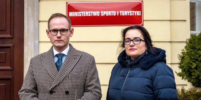 Na zdjęciu widać dwóch ludzi stojących przed budynkiem Ministerstwa Sportu i Turystyki.