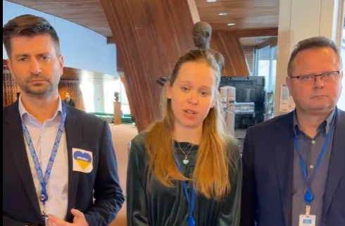 Na zdjęciu widać trzech ludzi stojących w pomieszczeniu, z widocznymi elementami wnętrza, w tym rzeźbą w tle.