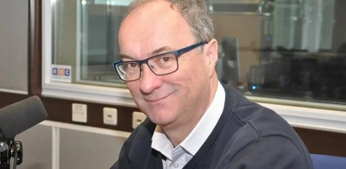 Uśmiechnięty mężczyzna w okularach siedzi przy mikrofonie w studiu radiowym.