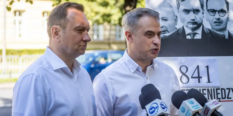 Dwóch mężczyzn w białych koszulach udziela konferencji prasowej przed mikrofonami, w tle widoczny plakat z twarzami, w kontekście incydentu z udziałem Black Hawk.