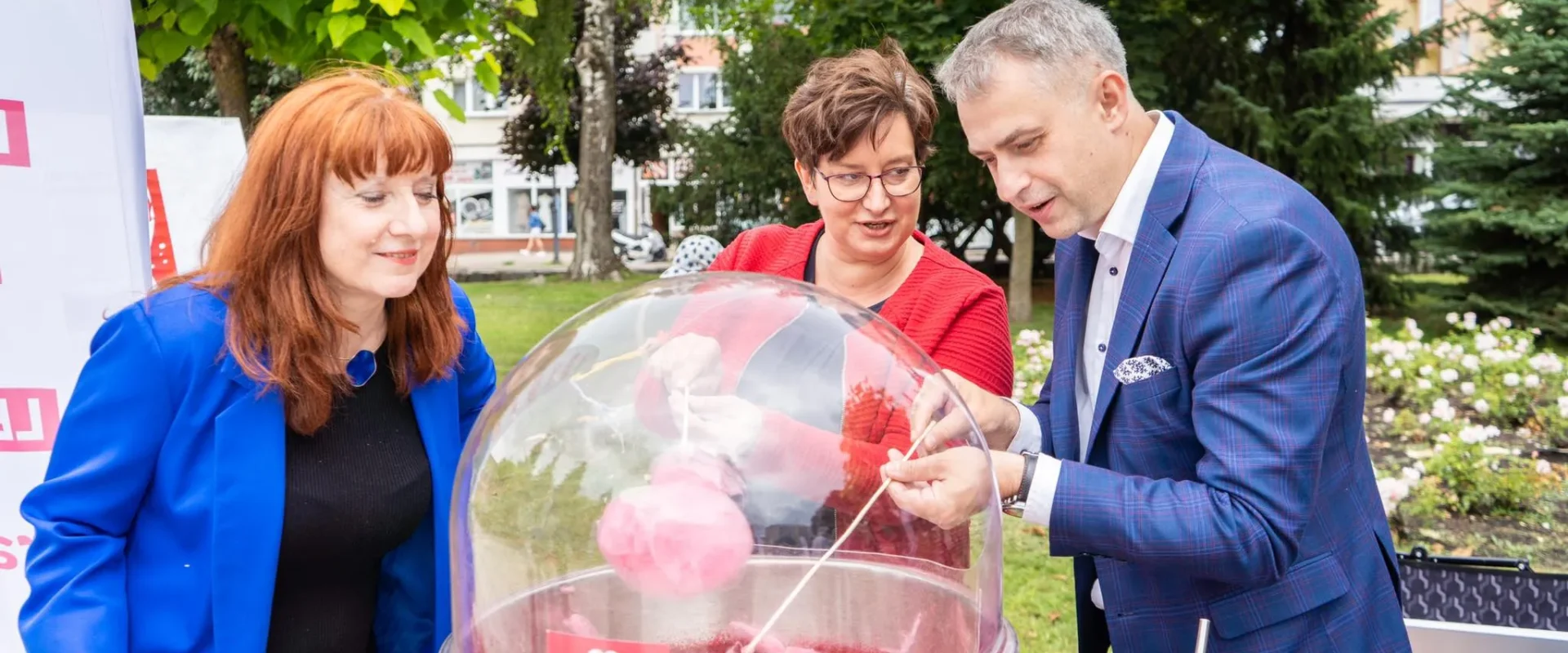 Trzy osoby stoją w parku przy maszynie do waty cukrowej podczas wydarzenia Trasa Bezpieczna Rodzina.