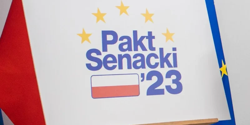 Plakat na sztaludze z napisem „Pakt Senacki ’23”, otoczony żółtymi gwiazdami, stoi między flagą Polski a flagą Unii Europejskiej.