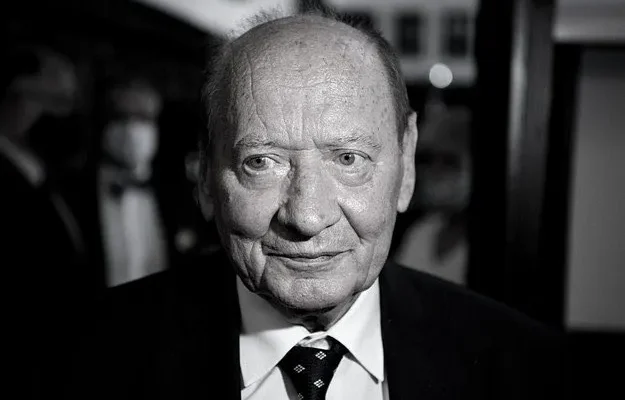 Na zdjęciu znajduje się starszy mężczyzna w garniturze, który patrzy w obiektyw aparatu w czarno-białej tonacji.