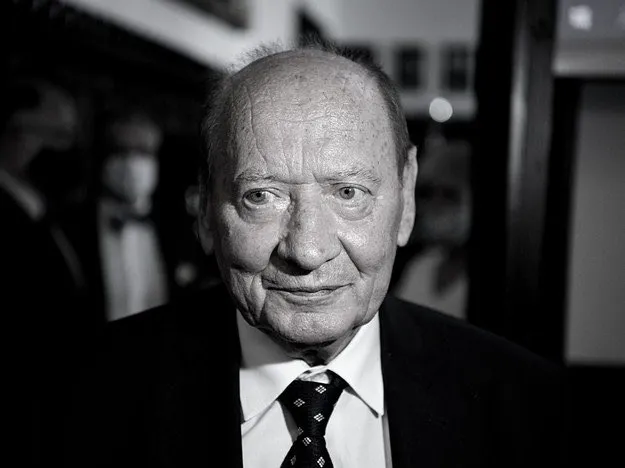 Na zdjęciu znajduje się starszy mężczyzna w garniturze, który patrzy w obiektyw aparatu w czarno-białej tonacji.