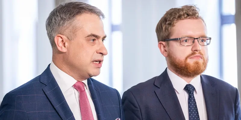 Dwóch mężczyzn w garniturach stoi w biurze podczas formalnego spotkania.