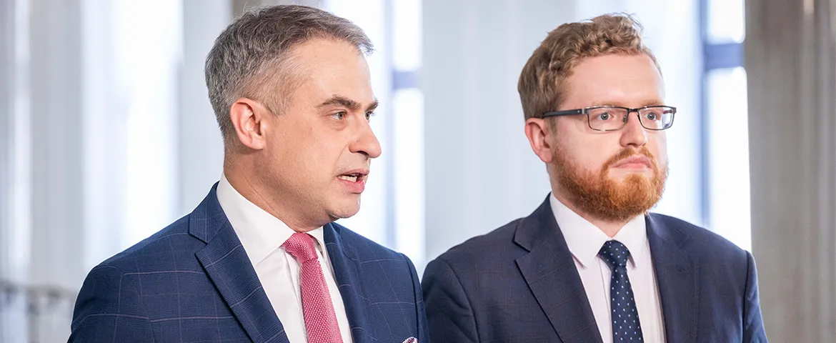 Dwóch mężczyzn w garniturach stoi w biurze podczas formalnego spotkania.