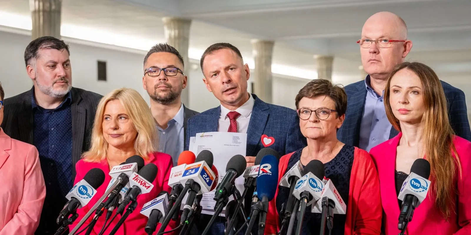 Grupa polityków na konferencji prasowej stoi za licznymi mikrofonami, trzymając dokumenty, w kontekście zawiadomienia do prokuratury w sprawie bezprawnego zwołania Komisji Edukacji, Nauki i Młodzieży.