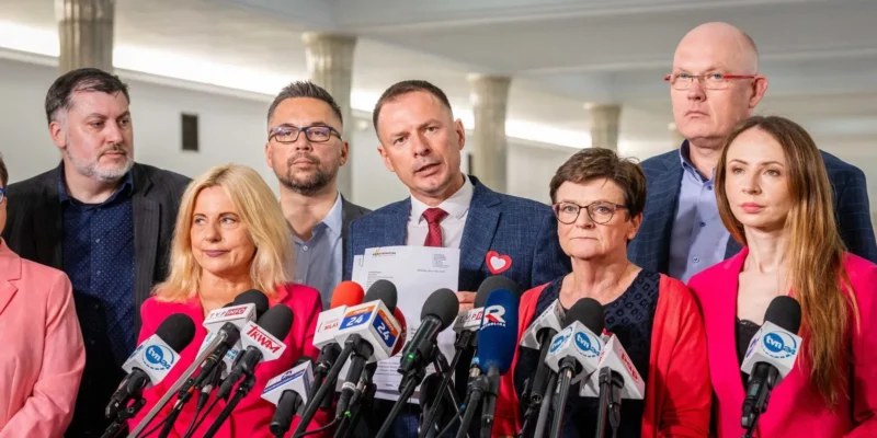 Grupa polityków na konferencji prasowej stoi za licznymi mikrofonami, trzymając dokumenty, w kontekście zawiadomienia do prokuratury w sprawie bezprawnego zwołania Komisji Edukacji, Nauki i Młodzieży.