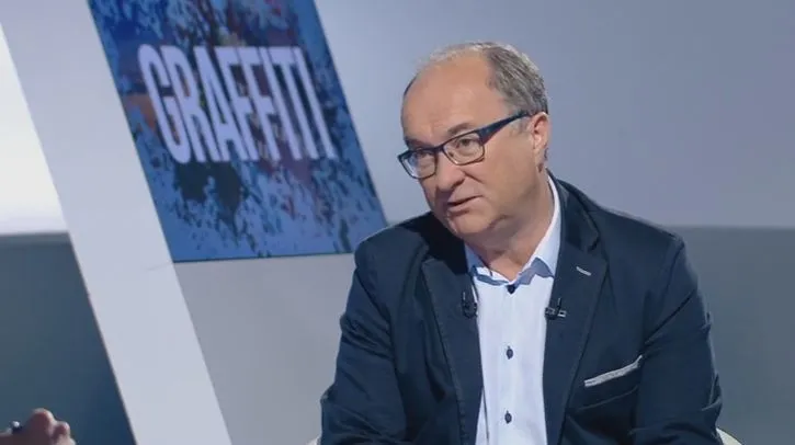 Mężczyzna w marynarce i okularach siedzi w studiu telewizyjnym i wypowiada się o miesięcznicach smoleńskich.